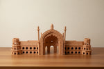 A small wooden architectural model of Rumi Darwaja, Lucknow a domed palace or mosque with minarets, displayed on a wooden table in an indoor room.